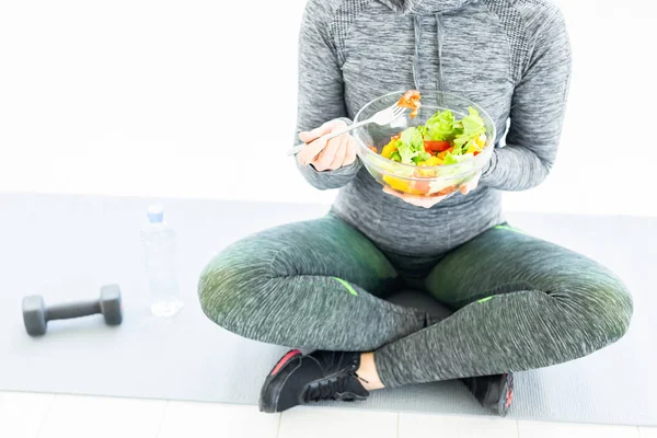 Sport, stile di vita sano e concetto di persone - giovane donna con insalata e un manubrio seduta sul pavimento — Foto Stock