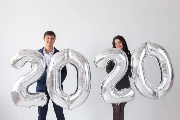 Año nuevo, celebración y concepto de vacaciones - pareja de amor divirtiéndose con signo 2020 hecho de globos de plata para el año nuevo sobre fondo blanco — Foto de Stock