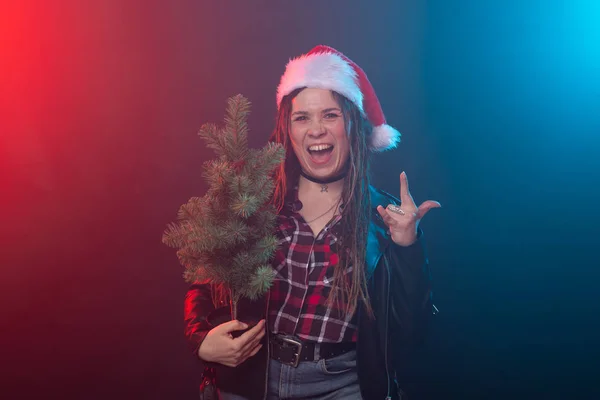 Natal, rock, estúdio, conceito de pessoas - jovem mulher em chapéu de Natal com pequena árvore de Natal sobre o fundo escuro — Fotografia de Stock