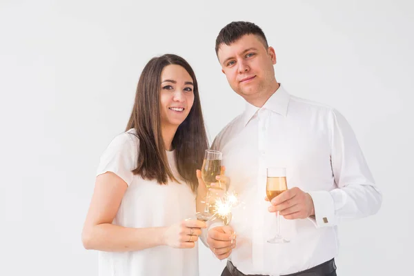 Ano Novo, feriados, data e dia dos namorados conceito - casal amoroso segurando faíscas luz e copos de champanhe sobre fundo branco — Fotografia de Stock