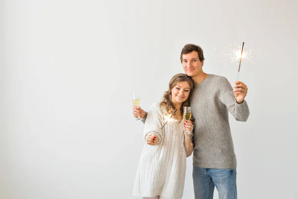 Ano Novo, feriados, data e dia dos namorados conceito - casal amoroso segurando faíscas luz e copos de champanhe sobre fundo branco com copyspace — Fotografia de Stock