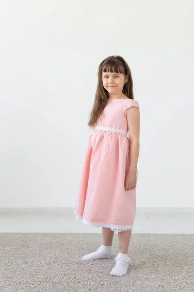 Vacker liten brunett flicka i en rosa klänning poserar på en vit bakgrund. Begreppet söta barn. Kopiera utrymme — Stockfoto
