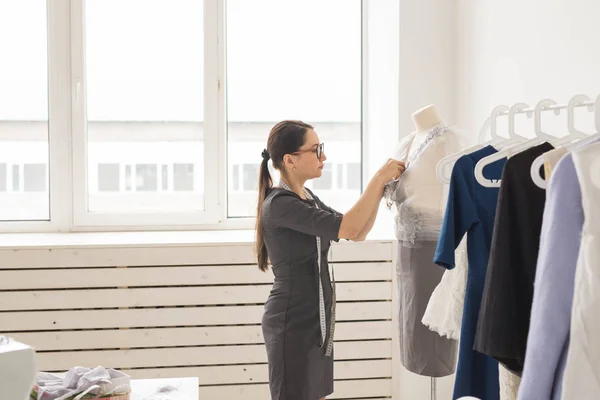 Dressmaker, tailor, fashion and showroom concept - Side view of female fashion designer measuring materials on mannequin in office