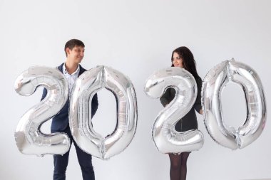 Yeni yıl, kutlama ve tatil konsepti - beyaz arka plan üzerinde yeni yıl için gümüş balonlardan yapılmış 2020 işareti ile eğlenen aşk çift