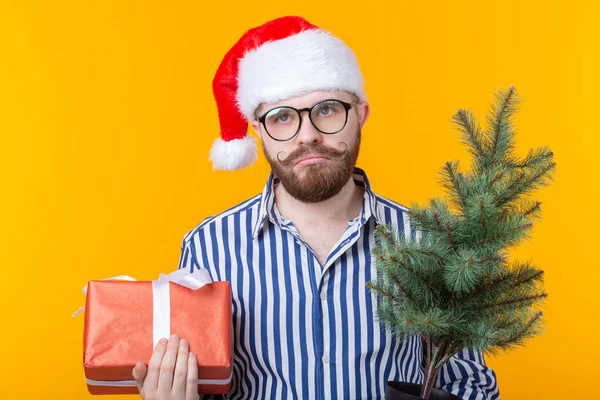 Pozytywny młody człowiek Święty Mikołaj z prezentów i choinki stwarzających na żółtym tle. Koncepcja świąt Bożego Narodzenia i nowego roku. — Zdjęcie stockowe