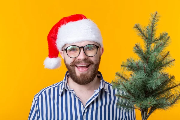 Positiv ung man jultomten med julgran poserar på en gul bakgrund. Jul-och nyårshelgen Concept. — Stockfoto