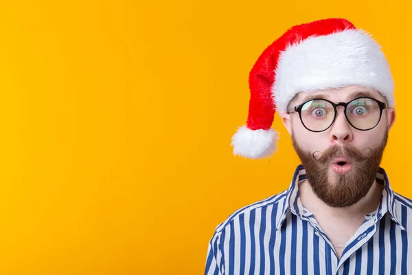 Verraste jonge man Kerstman die naar de camera op een gele achtergrond kijkt. Het concept van felicitaties voor het nieuwe jaar en Kerstmis. Advertentieruimte. — Stockfoto