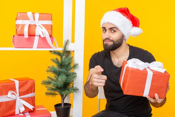 戴着圣诞老人帽子的年轻帅哥在圣诞树旁拿着祝贺礼物。圣诞节和新年假期的概念. — 图库照片