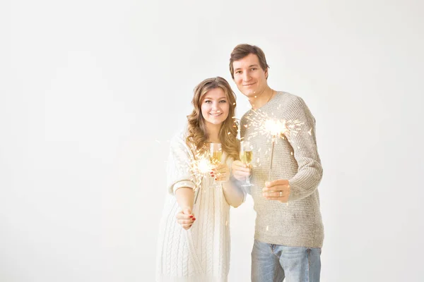 Ano Novo, feriados, data e dia dos namorados conceito - casal amoroso segurando faíscas luz e copos de champanhe sobre fundo branco com espaço de cópia — Fotografia de Stock