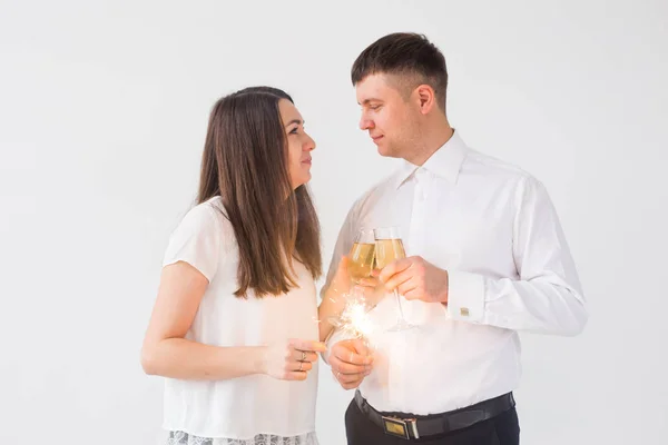 Ano Novo, feriados, data e dia dos namorados conceito - casal amoroso segurando faíscas luz e copos de champanhe sobre fundo branco — Fotografia de Stock