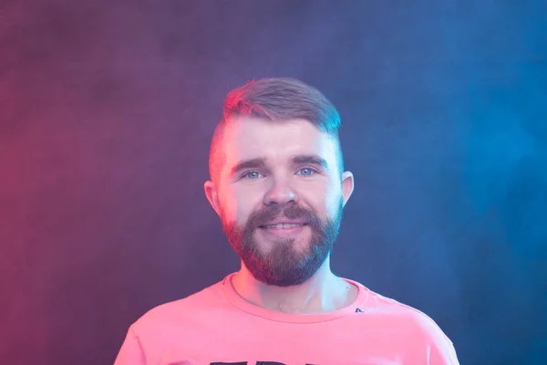 Jovem hipster homem moderno positivo com uma barba de bigode na camisa posando em um fundo azul . — Fotografia de Stock