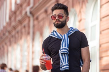 Şık bir bıyık ve elinde meyve suyu ile bir sakal ile yakışıklı neşeli genç arap öğrenci, bir iş gününden sonra şehir etrafında yürüyüş. Pozitif ve dinlenme kavramı.