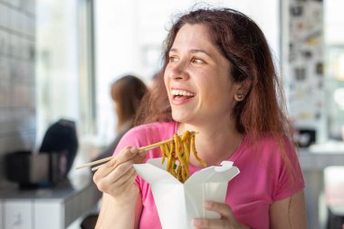 Bir kafede oturan ahşap çubuklarla Çin eriştesi yiyen genç güzel kızın yakın çekim portresi. Açlık ve tokluk kavramı.