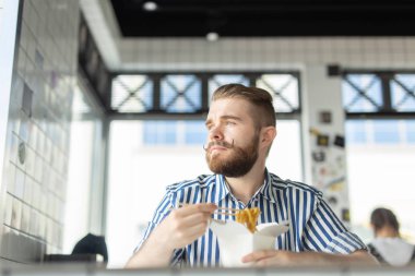 Yakışıklı genç hipster adam bir kafede oturan ve pencereye bakarak ahşap çubukları kullanarak Çin erişte yeme. Asya mutfağı konsepti.