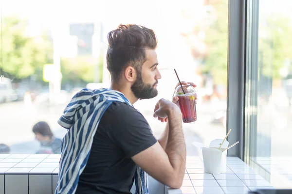 Guapo joven hipster bebiendo cóctel en un café y mirando por la ventana . — Foto de Stock