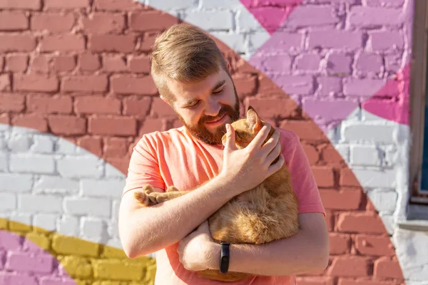 애완 동물 소유자와 우정 개념 - 잘 생긴 남자는 귀여운 생강 고양이를 잡고 포옹하고 있습니다. 호기심이 많은 표정을 가진 고양이 — 스톡 사진