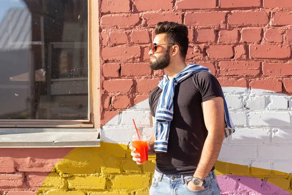 Schattig stijlvolle Arabische jonge mannelijke hipster met een snor en een baard en het dragen van glazen drinken sap met een rietje. Zomer vakantie concept. — Stockfoto