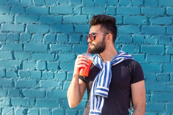 Retrato de un joven árabe alegre positivo con un vaso de jugo con una pajita mientras camina por la ciudad en un cálido día soleado de verano. El concepto de descanso después del estudio y el trabajo los fines de semana . — Foto de Stock