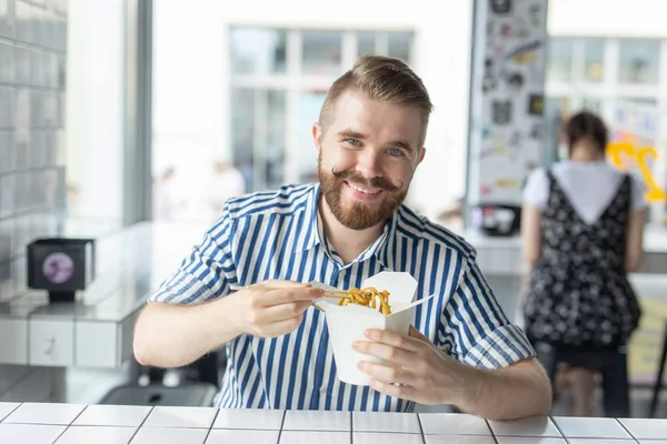 Positivo jovem elegante cara comendo macarrão chinês em um café durante uma pausa no trabalho. O conceito de descanso e lanche saudável . — Fotografia de Stock