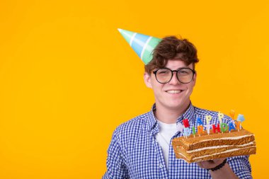 Elinde bir şapka ve sarı bir arka plan üzerinde poz bir ev yapımı kek ile Pozitif komik genç adam. Yıldönümü ve doğum günü konsepti.
