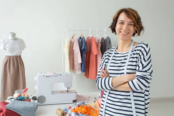 Portrait of a positive young woman seamstress cutter standing on the background of her desktop with her accessories and sewing machine. The concept of creating unique design products.