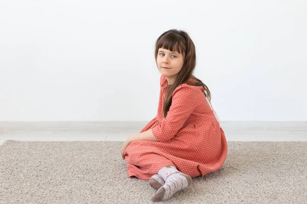 Niña linda sentada con un modesto vestido rosa largo contra una pared blanca. El concepto de niños pequeños e inocentes . — Foto de Stock