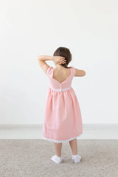 Vista trasera de una encantadora princesa niña en un vestido rosa posando en un vestido de diseñador sobre un fondo blanco. El concepto de ropa infantil. Copiar espacio — Foto de Stock