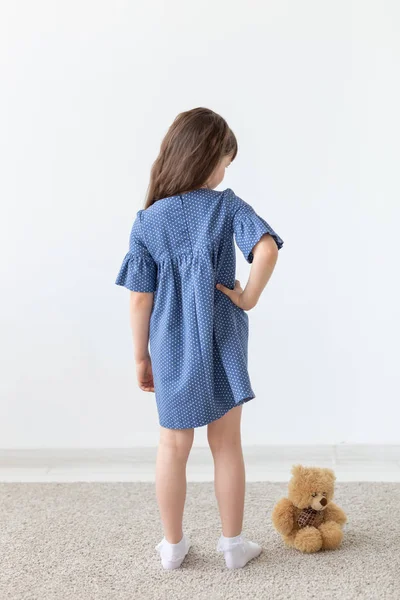 Charmig liten flicka poserar i blå polka dot klänning på en vit bakgrund. Konceptet med klassiska barnkläder och snygga barn. — Stockfoto