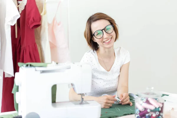 Jeune jolie étudiante étudie chez un designer de vêtements à l'université et fait sa première thèse assise à un bureau avec une machine à coudre. Concept de conception de vêtements . — Photo