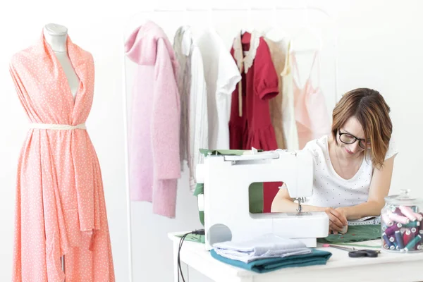 Jeune jolie étudiante étudie chez un designer de vêtements à l'université et fait sa première thèse assise à un bureau avec une machine à coudre. Concept de conception de vêtements . — Photo