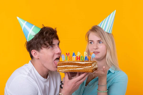 종이 모자를 쓴 기괴한 젊은 커플 소녀와 소년의 가까이에서 축하 케이크 한 조각을 물고 싶어합니다. 생일 및 축 하 컨셉. — 스톡 사진