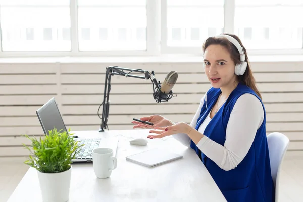 Concepto de presentador de radio - Mujer trabajando como presentadora de radio sentada frente al micrófono sobre fondo blanco en el estudio — Foto de Stock