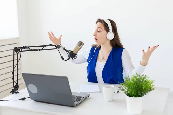 Concepto de presentador de radio - Mujer trabajando como presentadora de radio sentada frente al micrófono sobre fondo blanco en el estudio — Foto de Stock