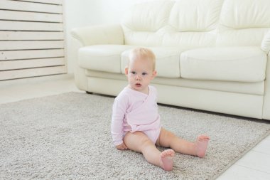 Küçük emekleme kız kız bir yaşında parlak ışık oturma odasında katta gülümseyerek ve gülüyor oturuyor. Evde oynayan mutlu bir çocuk. Çocukluk kavramı