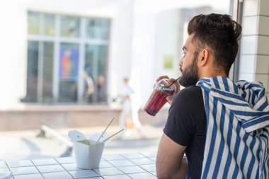 Yakışıklı genç hipster adam bir kafede kokteyl içme ve pencereye bakarak.