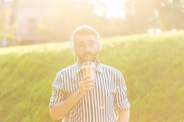 Sakallı, süt sallama lı ve sıcak bir yaz gününde parkta yürüyen şehrin manzarasına hayran olan şık bir genç adamın yan görünümü. Dinlenme ve rahatlama kavramı.