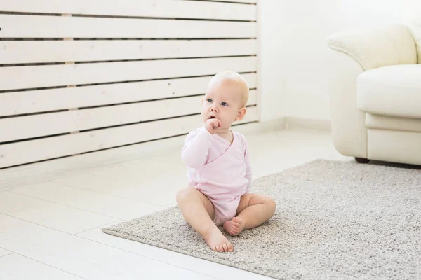 Childhood, children and babyhood concept - Adorable blonde baby sitting on the floor — Stock Photo, Image