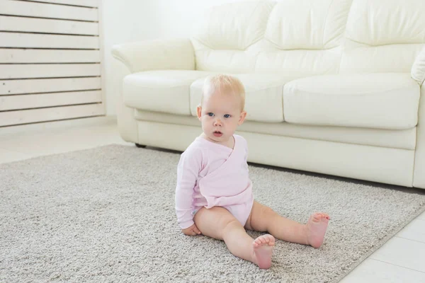 Küçük emekleme kız kız bir yaşında parlak ışık oturma odasında katta gülümseyerek ve gülüyor oturuyor. Evde oynayan mutlu bir çocuk. Çocukluk kavramı