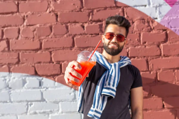 Guapo joven estudiante árabe alegre con un bigote elegante y una barba con jugo en las manos, caminando por la ciudad después de un día de trabajo. Concepto de positivo y descanso . — Foto de Stock