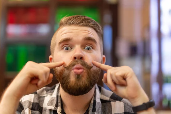 Chico hipster joven positivo lindo con un bigote y barba sonriendo posando en un café. El concepto de los hombres alegres divertidos . — Foto de Stock