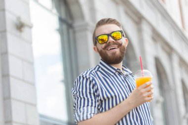 Şık bir bıyık ve elinde meyve suyu ile bir sakal ile oldukça neşeli genç işadamı yan görünümü, bir iş gününden sonra şehir etrafında yürüyüş. Pozitif ve dinlenme kavramı.