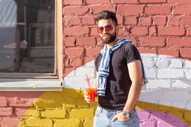 Şık bir bıyık ve elinde meyve suyu ile bir sakal ile yakışıklı neşeli genç arap öğrenci, bir iş gününden sonra şehir etrafında yürüyüş. Pozitif ve dinlenme kavramı.