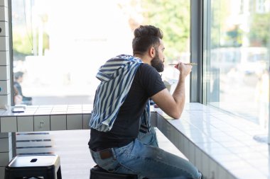 Yakışıklı genç hipster adam bir kafede oturan ve pencereye bakarak ahşap çubukları kullanarak Çin erişte yeme. Asya mutfağı konsepti.