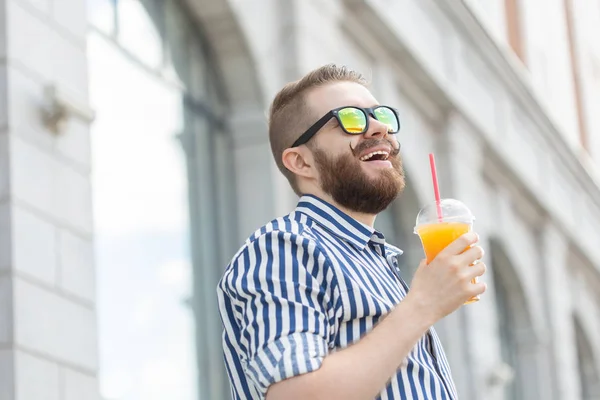 Zijaanzicht van een mooie vrolijke jonge zakenman met een stijlvolle snor en een baard met SAP in zijn handen, wandelen door de stad na een werkdag. Concept van positieve en rust. — Stockfoto