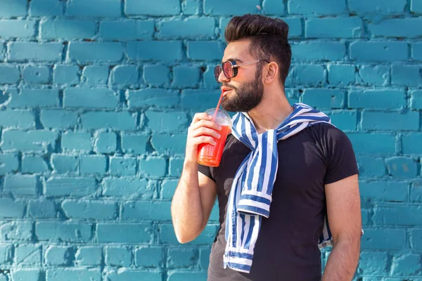 Schattig stijlvolle Arabische jonge mannelijke hipster met een snor en een baard en het dragen van glazen drinken sap met een rietje. Zomer vakantie concept. — Stockfoto