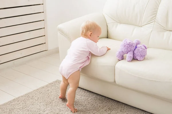 Childhood, babyhood and people concept - happy little baby girl playing near couch at home — Stock Photo, Image