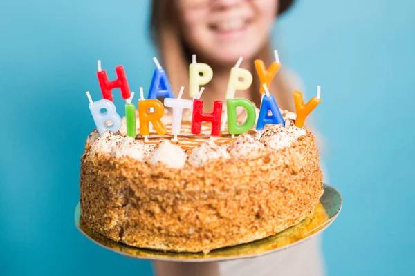 Mavi arka planda büyük bir Doğum günü pastası tutan bir kağıt şapka ve gözlük çılgın komik kız. Şaka ve selamlar kavramı. — Stok fotoğraf
