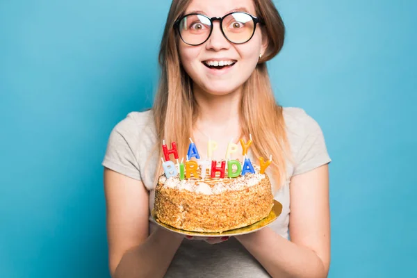 Bájos vidám őrült fiatal lány diák gratuláló papír kalap gazdaság boldog születésnapi torta a kezében állva ellen kék háttérben. Reklámfelület. — Stock Fotó