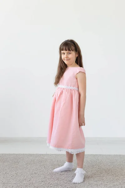 Vacker liten brunett flicka i en rosa klänning poserar på en vit bakgrund. Begreppet söta barn. Kopiera utrymme — Stockfoto