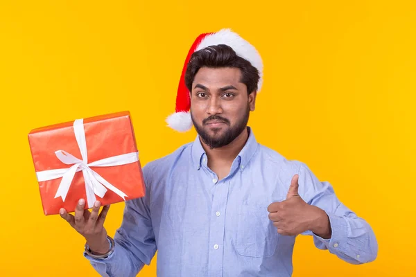 선물과 크리스마스 트리 노란색 배경에 포즈와 긍정적 인 젊은 인도 남자 산타 클로스. 크리스마스와 연말 연시 컨셉. — 스톡 사진